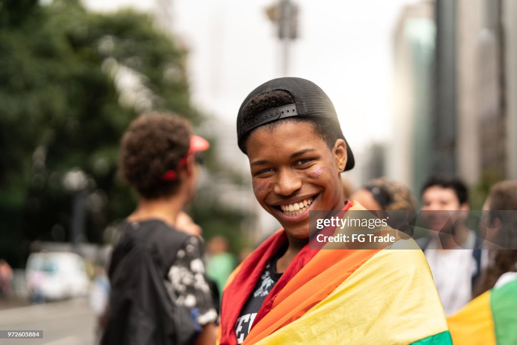 Portrait of young man with rainbow flag with friends on background at Gay Parade