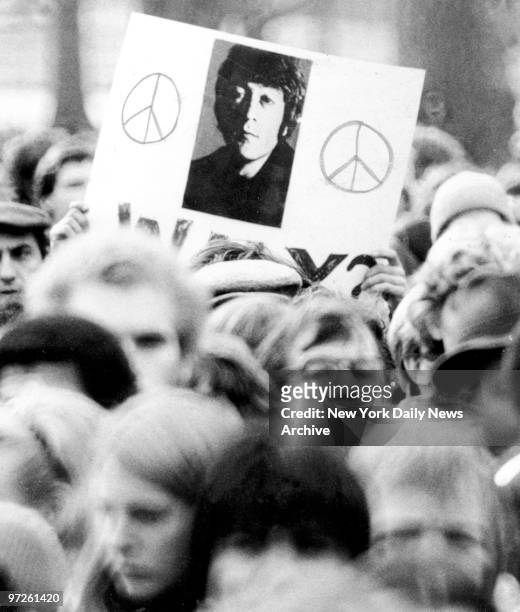 Fan holds a photo of John Lennon as crowd gathers to mourn his death.