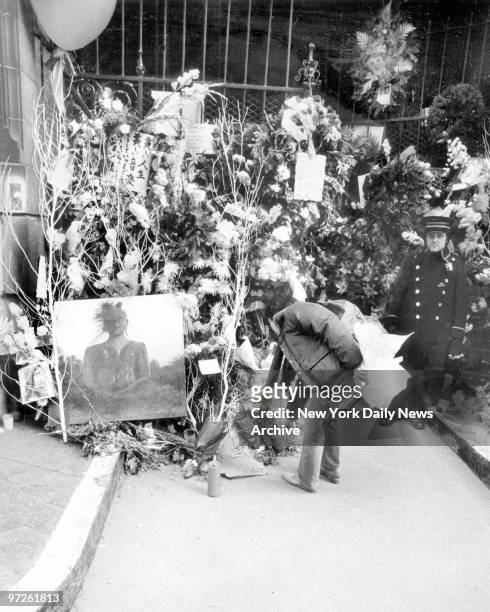 Mourner places bouquet among other items including an oil painting arrayed outside the Dakota apartments on 72d St. And Central Park West, where John...