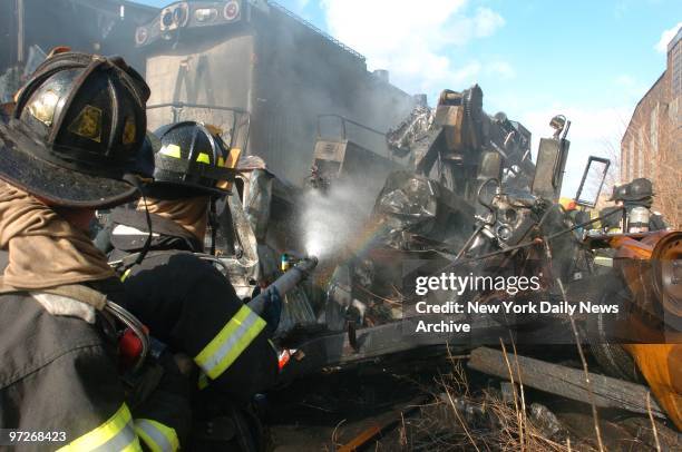 Firefighters play a hose on the tangled wreckage of a truck after it was hit by a runaway locomotive in Maspeth, Queens. An unmanned locomotive broke...