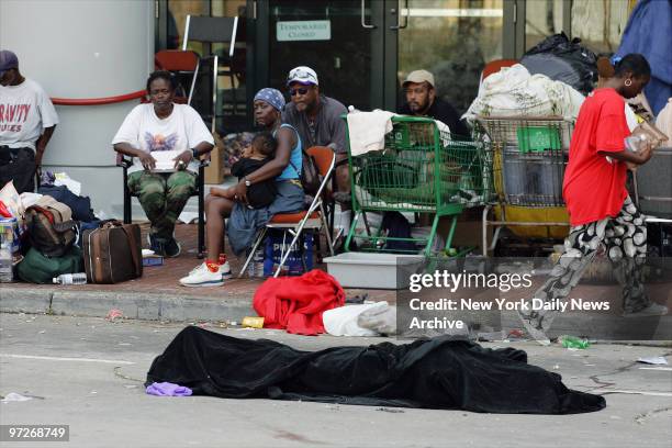 The body of a man, covered by a blanket, lies in the street as members of his family, driven from their homes by Hurricane Katrina, wait outside the...
