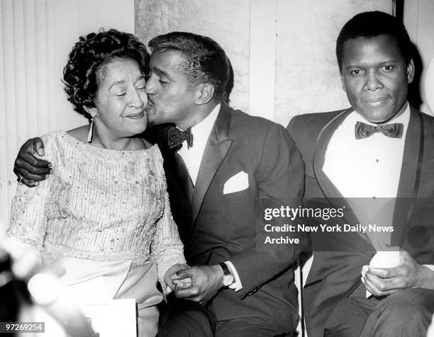 Sammy Davis, Jr. Gives his mother a kiss during a Friars Club dinner held in his honor at the Waldorf-Astoria. At right is Sidney Poitier.