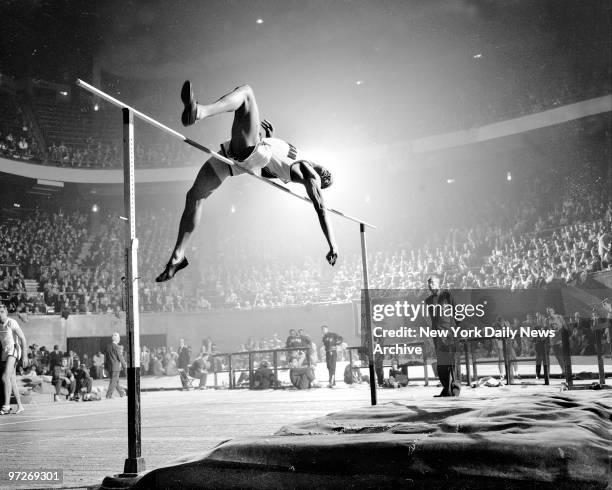 Morgan State's Bob Barksdale grimaces as he swings his body over bar set at 6'9" in high jump event at the Madison Square Garden. Official at right...