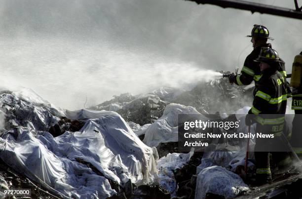 Firefighter sprays water on smoldering remains of American Airlines flight 587 after it crashed in the Rockaway section of Queens. White sheets cover...