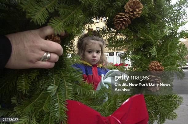 It's beginning to look a lot like Christmas to 2-year-old Addy Brennan, framed in wreath as she shops with her parents on Clinton St. In Carroll...