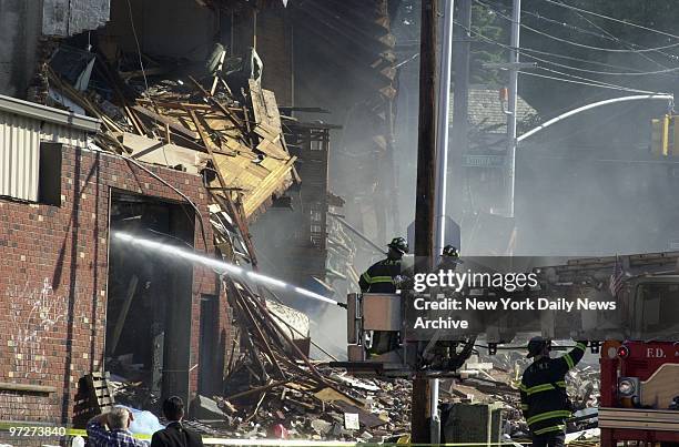Firefighters train hose on still-smoldering rubble at scene of five-alarm fire and hardware store explosion that blew away the front of a two-story...