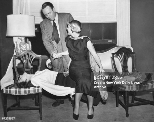 Mrs. Deems Taylor takes a seat on the rigid form of Lynne Faune , stretched between two chairs after she was hypnotized by Richard Kollmarr, who...