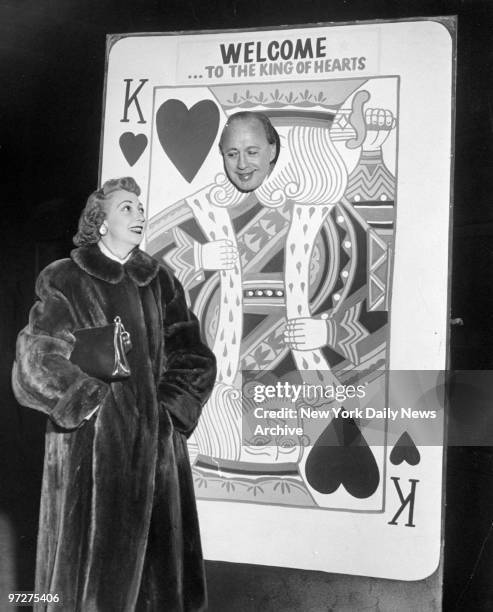 Jack Benny, known as the "King of Hearts", pokes his head through big playing card in Grand Central Station while wife Mary Livingstone looks on.