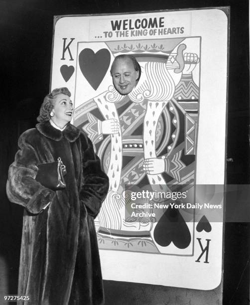 Jack Benny, known as the King of Hearts, pokes his head through big playing card in Grand Central Terminal while wife Mary Livingstone stands by.