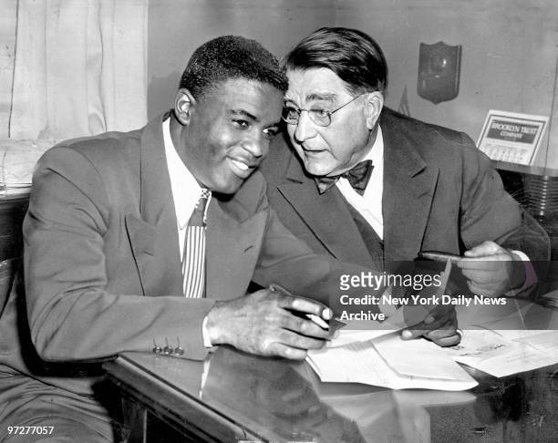 Jackie Robinson listens to Brooklyn Dodgers' owner Branch Rickey as Robinson signs a contract for $35 which made him the highest paid player in...
