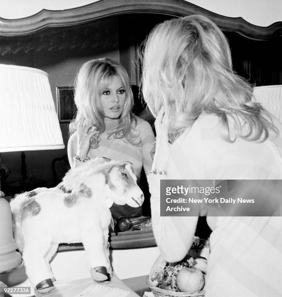 Brigitte Bardot checks her appearance in mirror at the Plaza Hotel. A doctor ordered dark glasses to protect her right eye, irritated by flashbulbs.