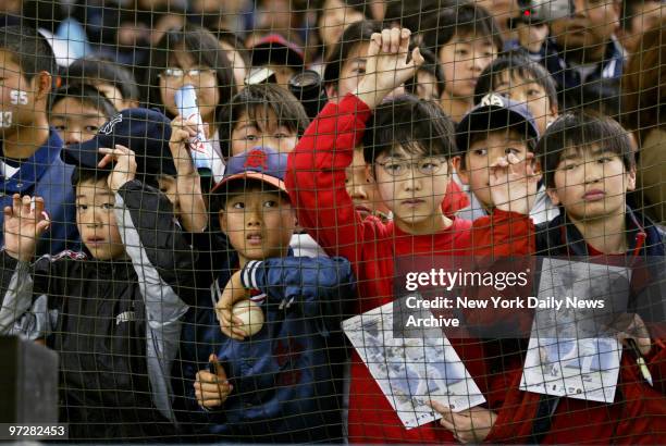 Japanese Little Leaguers, some holding pictures of New York Yankees' Hideki Matsui and one wearing his number on his cheek, watch from behind the...