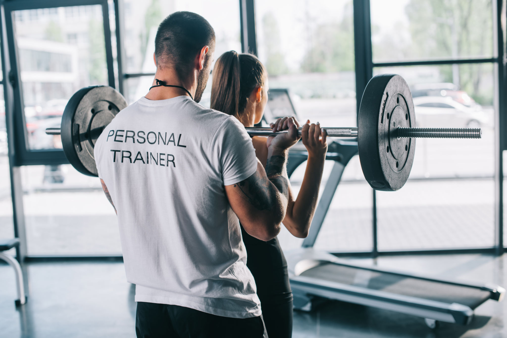 male personal trainer helping sportswoman to do exercises with barbell at gym male personal trainer helping sportswoman to do exercises with barbell at gym