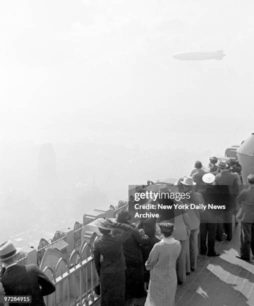 Spectators at the RCA building admire the Hindenburg dirigible as it glides over the city.