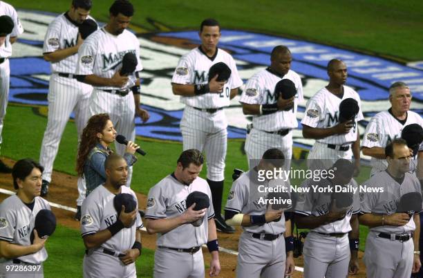 The New York Yankees and the Florida Marlins stand with heads bowed and their caps over their hearts as Gloria Estefan sings the National Anthem...