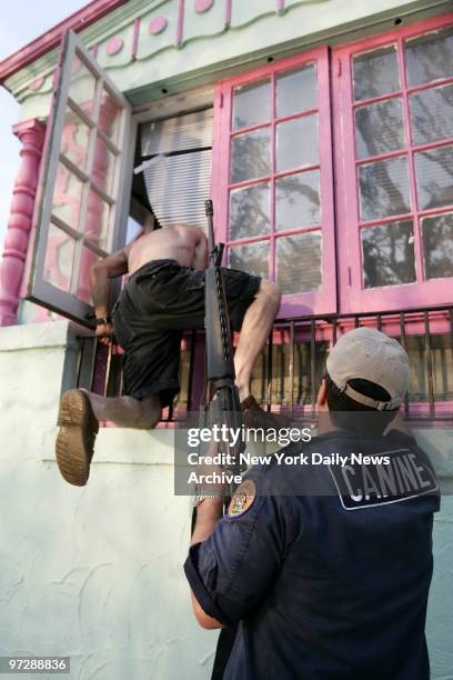 Capt. Eddie Hosli, commander of the 2nd District of the New Orleans Police Dept., holds an AR-15 rifle as a volunteer climbs in the window of a home...