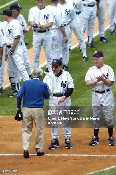 Former New York Yankees' shortstop Phil Rizzuto shakes hands with former Yanks' catcher and manager Yogi Berra as former Yankees' pitcher Whitey Ford...