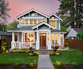 Beautiful luxury home exterior with glowing interior lights at sunset in suburban neighborhood
