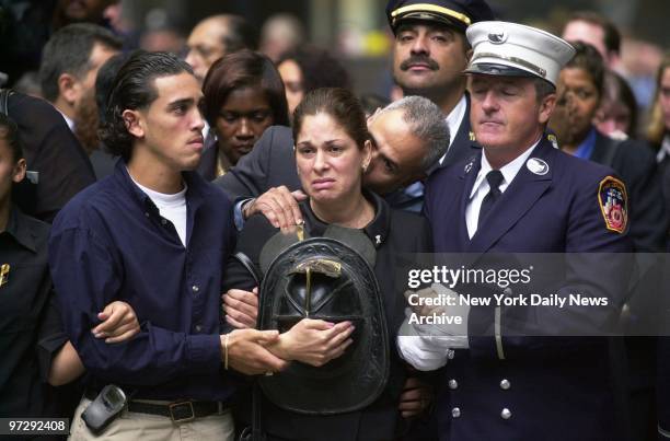 Maria Rivera, the fiance of fallen firefighter Lt. Dennis Mojica, holds his fire helmet tightly as she is comforted by firefighters and family during...