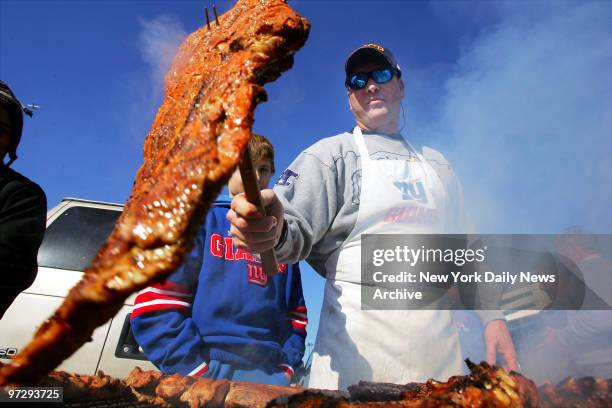 New Jersey State Trooper Chris Hughes flips a rack of ribs while tailgating before the start of the New Jersey Giants' game against the Philadelphia...