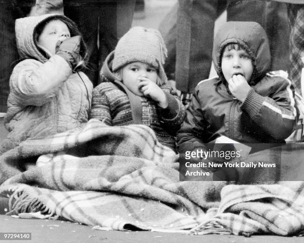 Three children keep their cool on the outside as blanket helps them ward off icy blasts while viewing Macy's Thanksgiving Day parade.