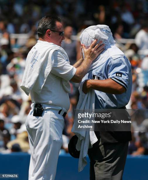 New York Yankees' head trainer Gene Monahan cools off home plate umpire Larry Poncino with a soaking-wet towel on a scorching August afternoon during...