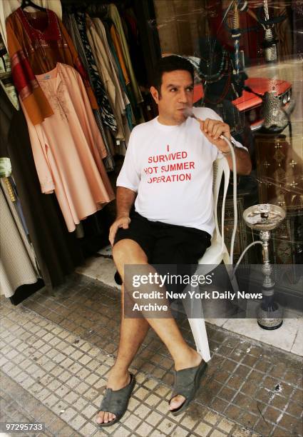 Shop owner Ammar smokes a water pipe outside his store in Central Beirut where he sells such items as T-shirts like the one he is wearing that reads,...