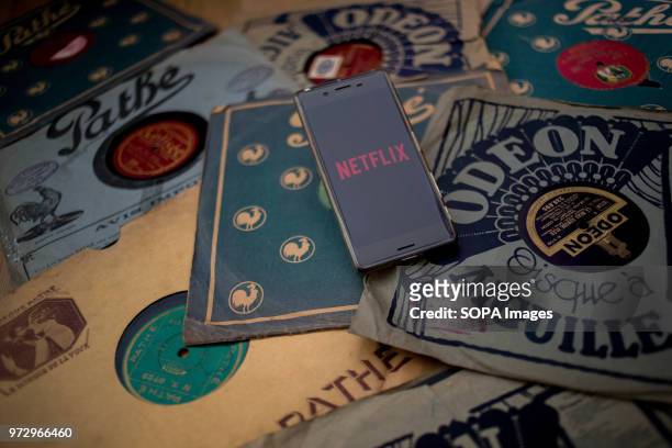 In this photo illustration, the Netflix application seen displayed via the Google Play Store on an Android Sony smartphone surrounded by old 78rpm...