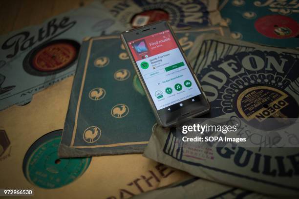 In this photo illustration, the Spotify application seen displayed via the Google Play Store on an Android Sony smartphone surrounded by old 78rpm...