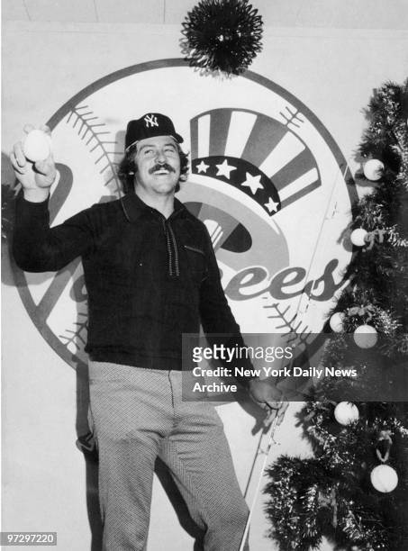 Jim "Catfish" Hunter rejoices after signing record contract with the New York Yankees at Shea Stadium. He stands at a baseball decorated Christmas...