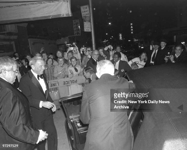 Frank Sinatra is cheered by adoring lady fans and clicking photographers as he approaches limousine occupied by his wife, Barbara, outside Carnegie...