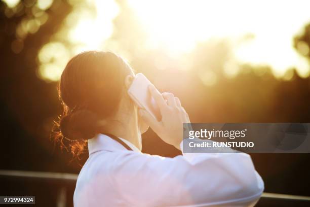 doctor talking on smartphone outdoors - healthcare worker beauty in nature stock pictures, royalty-free photos & images