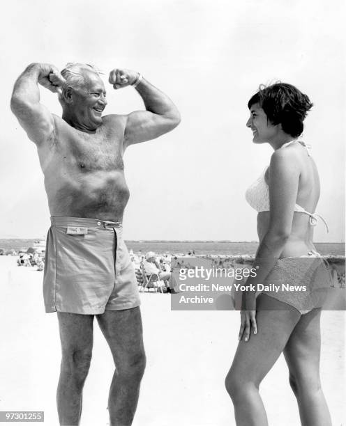 Charles Atlas who will be 75 years old in October, flexes his muscles outside his summer home in Point Lookout, L.I. Looking on with admiration is...