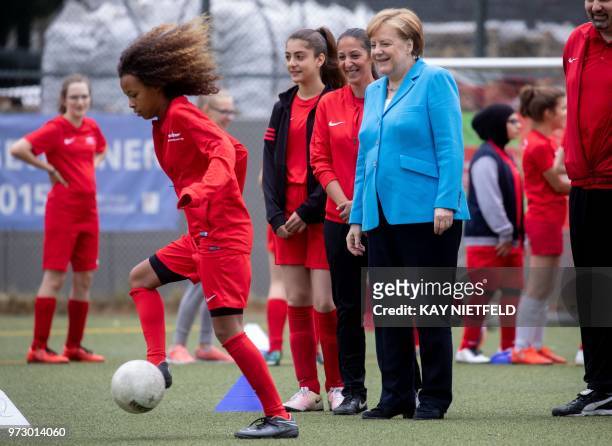 German Chancellor Angela Merkel looks at a girl playing football and taking part in the event "Sports and Integration" as she visits the "SV Rot-Weiß...