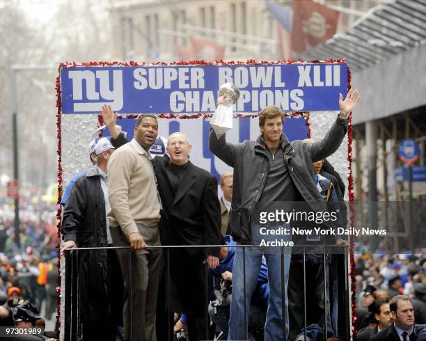 New York Giants' Eli Manning hold his team's Super Bowl trophy as he rides a float alongside head coach Tom Coughlin and Michael Strahan during the...