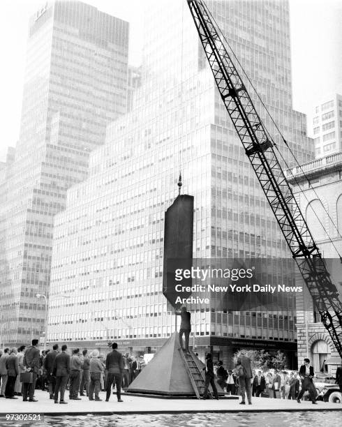 Three-ton sculpture, called the Broken Obelisk, is lowered by crane on its pedestal at Seagram Plaza. The 25-foot-high piece, created by Barnett...