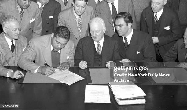 Joe Louis, who punches devastatingly with either hand, uses his right to sign for fight with Max Schmeling at Stadium, June 22. Gen. Phelan and Max...
