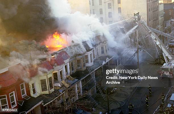 Smoke and flames rise from wooden row houses as firefighters atop aerial ladder direct streams of water onto blaze at College Ave. Near 169th St. In...
