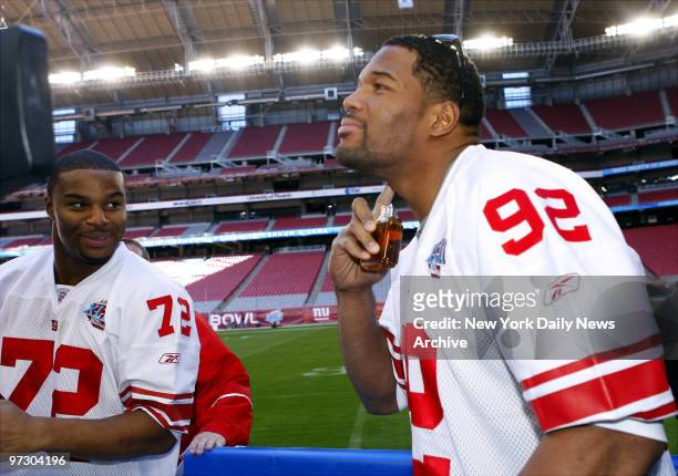 New York Giants' Osi Umenyiora looks on as teammate Michael Strahan samples a bit of Tom Brady for Stetson cologne during Media Day at the University...