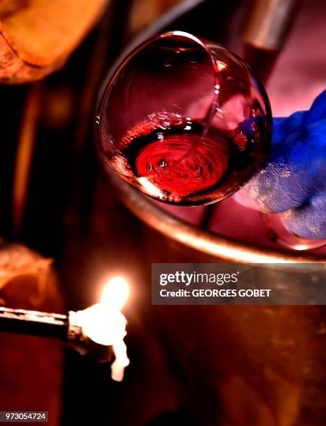 An employee uses the light of a candle to check the colour of wine in the wine cellar of Chateau Margaux on June 11, 2018 in Margaux, near Bordeaux,...