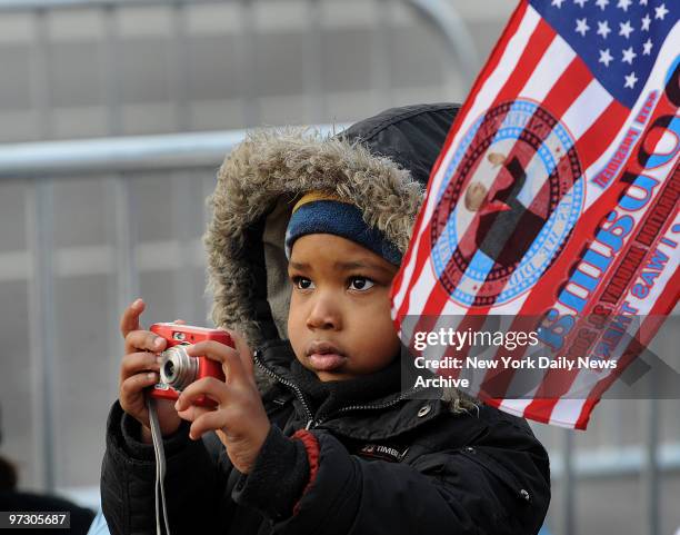 Child bundled up in a paarka holds up a camera to catch a ahot of the inaugural parade along Pennsylvania Ave.