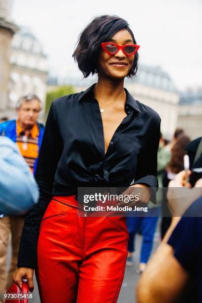 Model Jourdan Dunn wears red cat-eye sunglasses, a black silk knotted top, red moto leather pants during Paris Fashion Week Spring/Summer 2018 on...