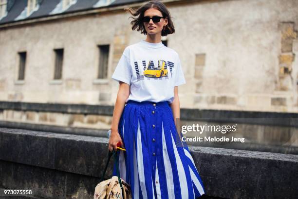 Model Giedre Dukauskaite wears black rectangular sunglasses, a KAR / L'Art de L'automobile car t-shirt, white and blue pleated skirt during Paris...