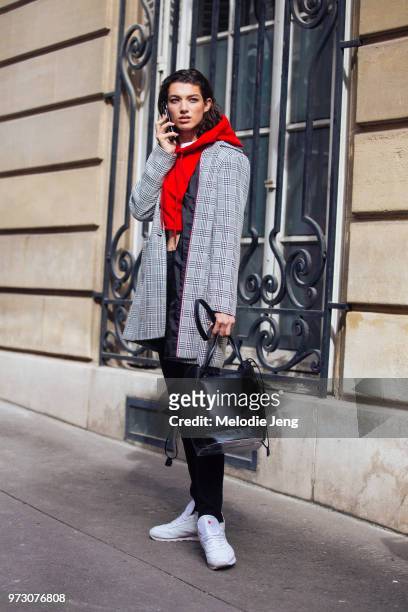 Model Mckenna Hellam talks on the phone and wears a gray plaid jacket, cropped red hoodie, black bat and pants, white Reebok sneakers during Paris...