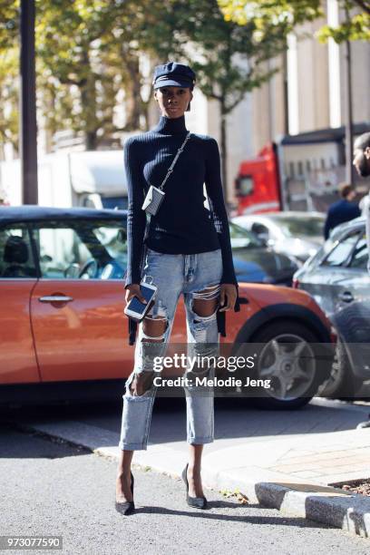 Model Tami Williams wears a blue newsboy cap, blue turtleneck sweater, miniature cross-body purse, distressed jeans, black heels during Paris Fashion...