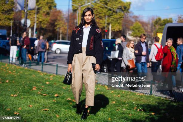 Brazilian model Gizele Oliveira in a black jacket with Paris-themed patches, tan pleated jodhpur pants, a black purse, and black boots during Paris...