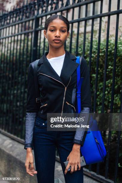 Model Naomi Chin Wing from Trinidad and Tobago wears a black biker-style jacket with mesh sleeves, blue Loewe bag, and blue jeans during Paris...