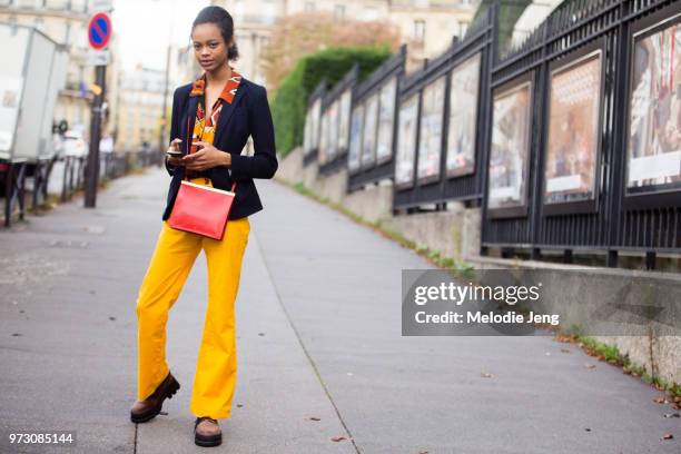 Model Aaliyah Hydes wears a black blazer, orange retro-style print shirt, red Celine bag, yellow orange pants, and chunky boots after Miu Miu during...