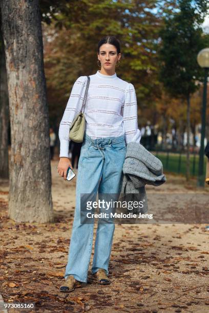 Brazilian model Cris Herrmann wears hoop earrings, a white top, blue jeans, a Chanel bag, and holds a Chanel jacket after the Chanel show during...