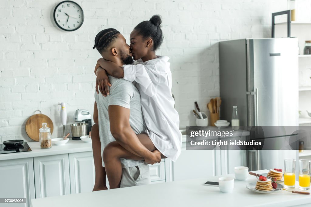Side view of african american boyfriend holding girlfriend and they kissing at kitchen